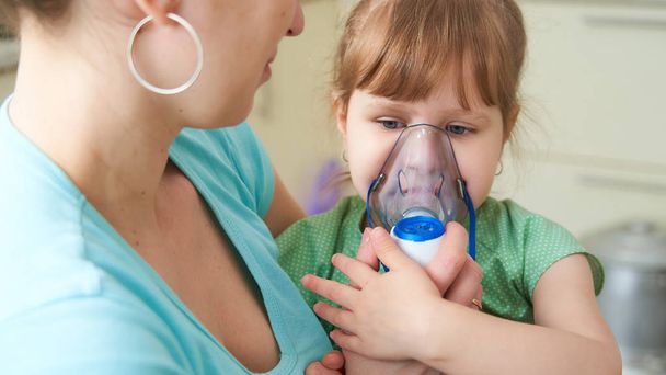 woman makes inhalation to a child at home. brings the nebulizer  - Photo, image