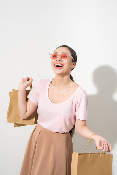 Hymyilevä nuori nainen pitelee ostoskasseja ja hymyilee kameralle, joka on eristetty valkoisella
 - Valokuva, kuva