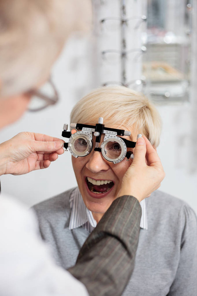 Mujer madura sonriente con examen de vista y medición de dioptrías en la clínica de oftalmología
 - Foto, Imagen
