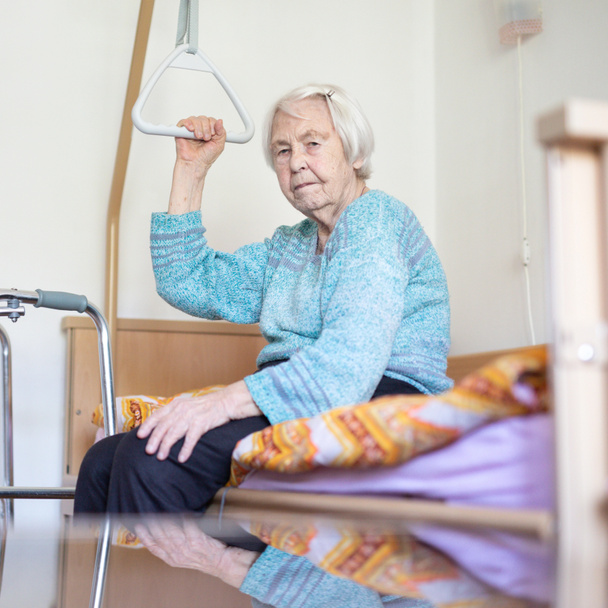 Starsi 96 lat kobieta siedzi na łóżku medycznym w hospic. - Zdjęcie, obraz