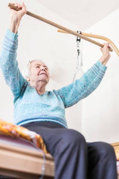 Ouderen 96 jaar oud vrouw oefenen met een stok zitten op haar slechte. - Foto, afbeelding