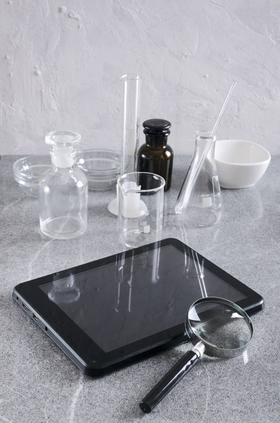 Vertical shot. Medical glassware, tablet and magnifier on the laboratory assistant workplace - Фото, изображение