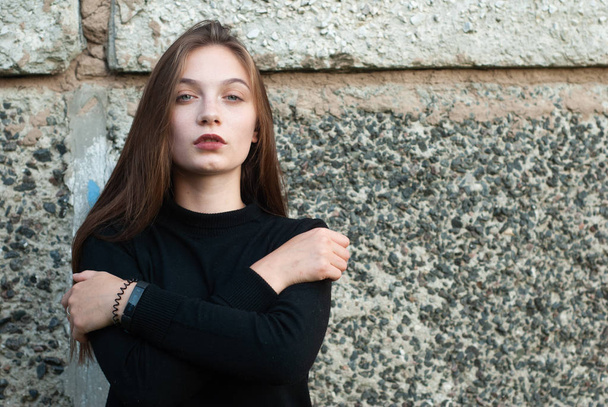 Mooi jong meisje in een zwarte coltrui trui poseren in de betonnen muur, - Foto, afbeelding