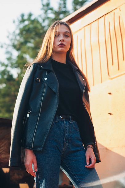 model in a black leather jacket and blue jeans posing outdoors. modern cool girl - 写真・画像