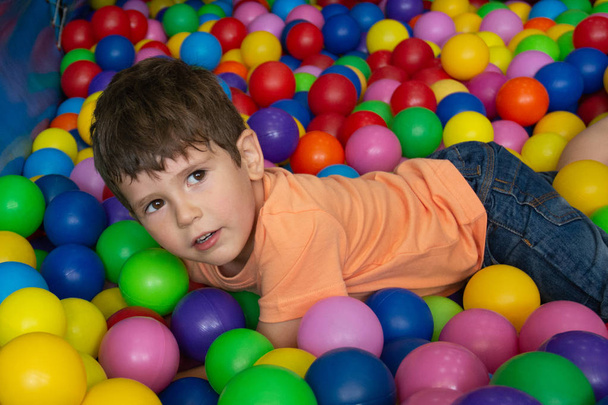 Ребенок играет с цветными мячами в бассейне для игры в мяч. Игрушки для детей. Детские эмоции счастья весело провести время в мяч яме на день рождения в парке развлечений детей или крытый игровой центр
. - Фото, изображение