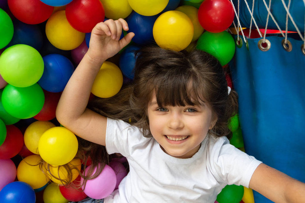 遊び場のボールプールでカラフルなボールで遊ぶ子供。小さな子供のための活動のおもちゃ。子供の遊園地や屋内プレイセンターで誕生日パーティーにボールピットで楽しむ子供の幸せ感情.  - 写真・画像
