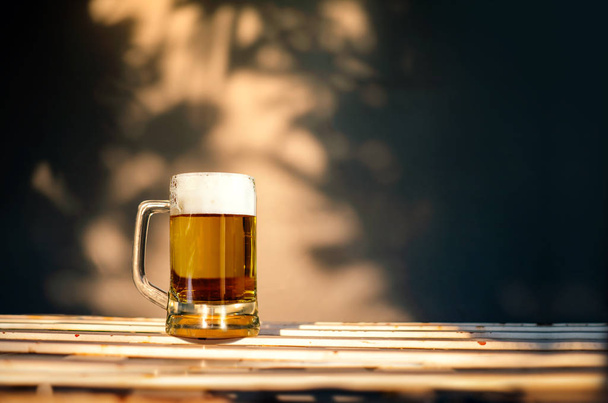 a Glass of Beer on Table in Summer Sunny Day. Shadow of Tree as  - 写真・画像