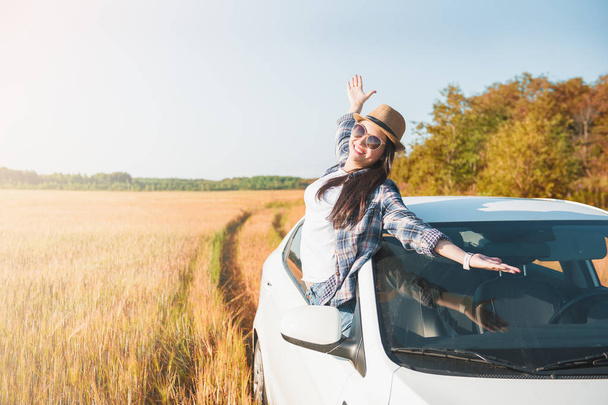 野原の白い車で手を挙げた若い女性  - 写真・画像