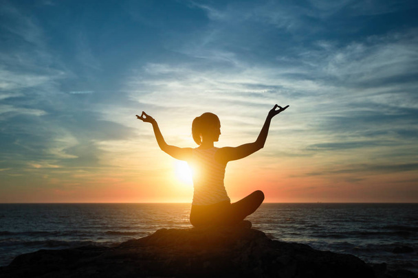Jooganainen meditoi Assanessa Lotus-asennossa. Siluetti meren rannikolla aikana kaunis auringonlasku
. - Valokuva, kuva
