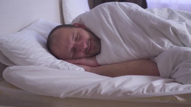 Sleeping man wakes up in a double bed. Side view, medium shot. - Video, Çekim