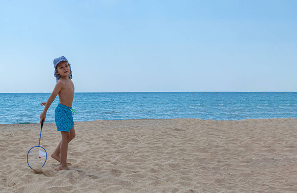 Ребенок играет с бадминтонной ракеткой и шаттлом на пляже. Концепция семейного отдыха. Копирование пространства
. - Фото, изображение