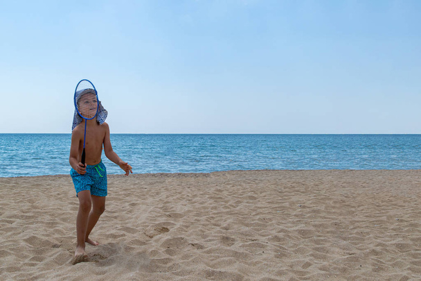 The child plays with a badminton racket and a shuttlecock on the beach. The concept of a family holiday. Copy space. - Foto, Bild
