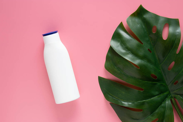cosmetic nature skincare concept. white cosmetic bottle container with blank label for branding mock up, decorate with green tropical leaves on pink background with copy space - Photo, Image
