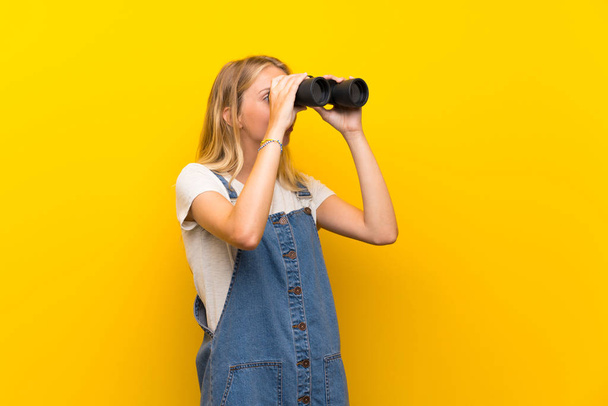 Blonďatá mladá žena na izolovaném žlutém pozadí s černým dalekohledem - Fotografie, Obrázek