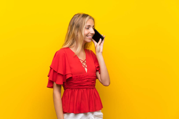 Cep telefonu kullanarak izole sarı arka plan üzerinde Sarışın genç kadın - Fotoğraf, Görsel