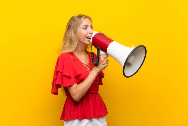 Blonde young woman over isolated yellow background shouting through a megaphone - Фото, зображення