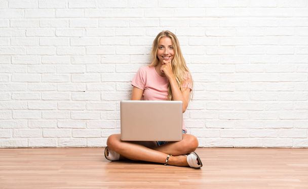 Young blonde student girl with a laptop on the floor laughing - Photo, Image