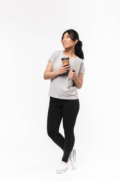 Asian beautiful young woman posing isolated over white wall background drinking coffee holding laptop computer. - Photo, image