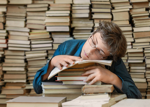 Sleeping boy as a pupil in the library with a big stack of books. Close up portrait. - Photo, Image