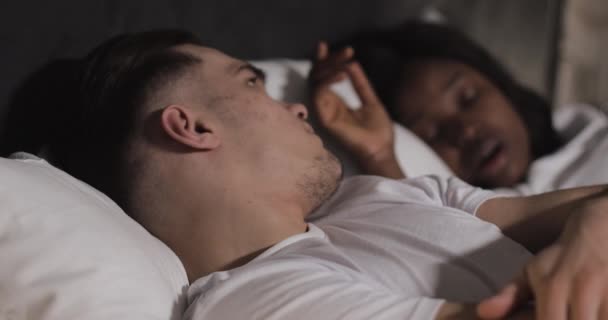 Multi-ethnic couple lying in bed together. Man suffers from his partner snoring in bed. Couple lifestyle and people health care concept. - Filmati, video