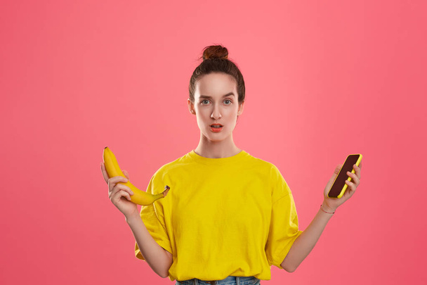 Sarı bir t-shirt tutan muz ve sarı Smartphone bir saç topuz ile model - Fotoğraf, Görsel