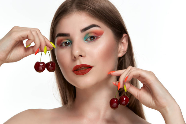 顔の近くにイチゴを保持する明るい色のメイクアップを持つ美しい若い女性のクローズアップ肖像画. - 写真・画像