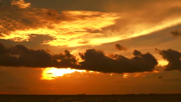 zonsondergang oranje gele hemel en donker rode wolk bewegen op zee en silhouet vrachtschip parkeren - Video