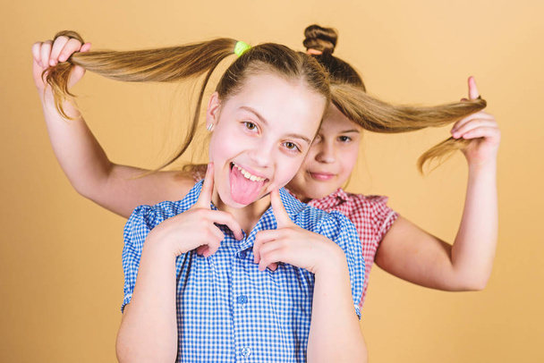 Natural hair extensions. Little child keeping long hair of her sister. Small girl smiling with blond hair. Cute happy kid with fashionable hair ponytails - Фото, зображення
