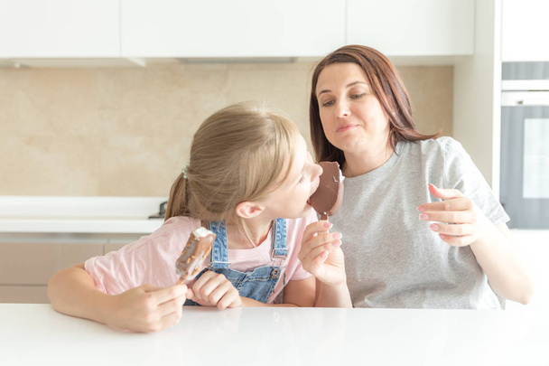 Moeder met dochter in keuken eten ijs. Goede relaties van ouder en kind. Gelukkig familieconcept - Foto, afbeelding
