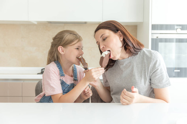 Moeder met dochter in keuken eten ijs. Goede relaties van ouder en kind. Gelukkig familieconcept - Foto, afbeelding