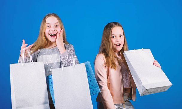 Kid fashion. Blue background. Sales and discounts. Small girls with shopping bags. Happy children. Little girl sisters. Sisterhood and family. savings on purchases. discounts. discounts concept - 写真・画像