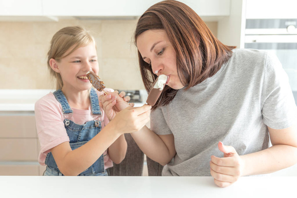 Мать с дочерью на кухне едят мороженое. Хорошие отношения родителей и детей. Концепция счастливой семьи
 - Фото, изображение