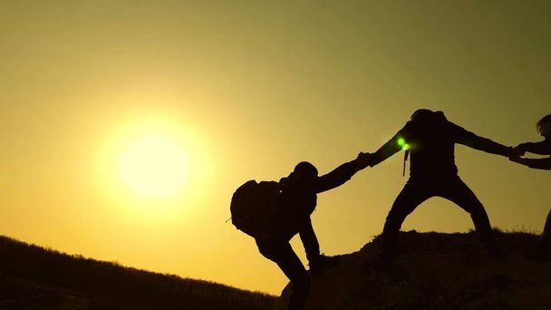 Teamwork der Geschäftsleute. Die Reisenden klettern nacheinander auf Felsen. Gemeinsame Sache. Zeitlupe. Bergsteiger Silhouetten strecken ihre Hände zueinander und klettern auf die Spitze des Hügels. - Foto, Bild