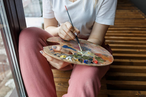 パレットの色を混ぜ合わせたブラシでアーティストの手をクローズアップ。アート、創造性、趣味. - 写真・画像