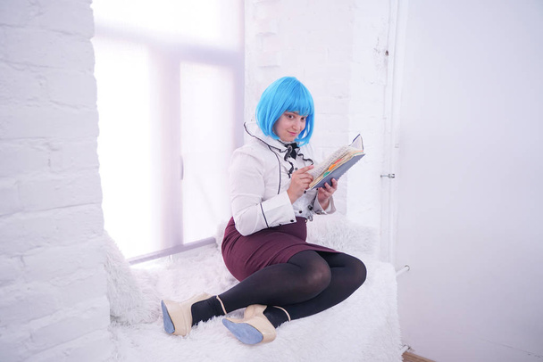 pretty plus size girl in blue wig have many dreams with her diary alone sitting on white windowsill - Foto, imagen