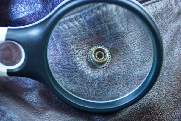 black magnifier magnifies a metal rivet on brown leather clothes - Photo, Image