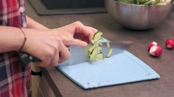 Young housewife slices cucumbers on plastic board - Filmati, video