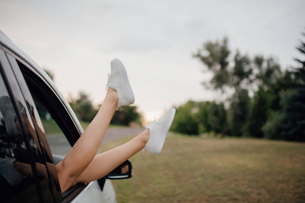 Female legs dangling from car window with a sky on background, outdoor - Photo, image