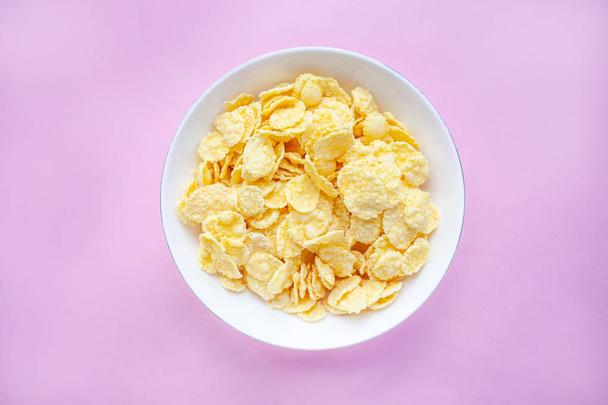 Cornflakes dry breakfast in a white bowl on a pink backgroud. top view - Fotografie, Obrázek