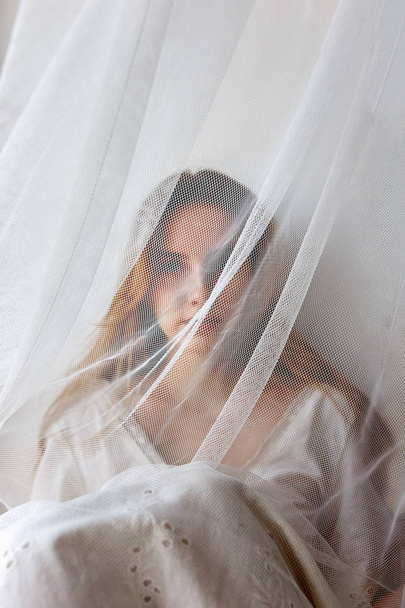Pretty young sensual girl in white dress hiding behind curtain. Hidden beauty concept - Zdjęcie, obraz