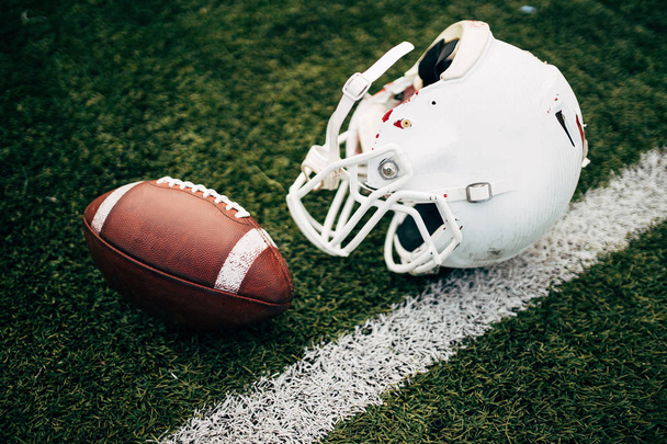 Photo of white helmet of Amerinian football player and ball on green lawn - Valokuva, kuva