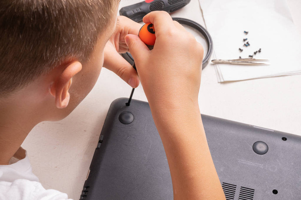 Um menino de 10 anos está classificando um laptop para limpeza e manutenção
 - Foto, Imagem