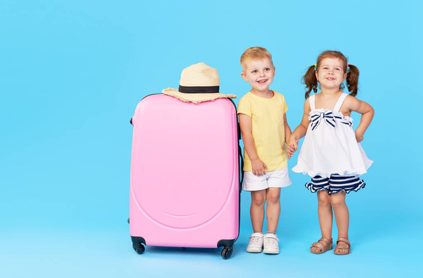 Happy kids sitting on colorful pink suitcase prepared for summer vacation. Young travelers. Little girl and boy, sister and brother, having fun isolated on blue background - Φωτογραφία, εικόνα