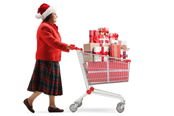 Elderly woman with a santa claus hat walking with a shopping car - Фото, изображение