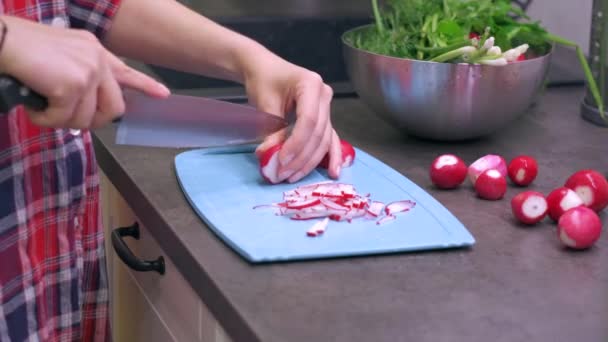 Young woman cuts radish on plastic cutting board - Filmati, video