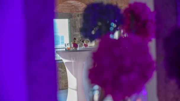 Bellissimi fiori enormi rosa e viola in primo piano e una tavola rotonda ben decorata sullo sfondo
. - Filmati, video