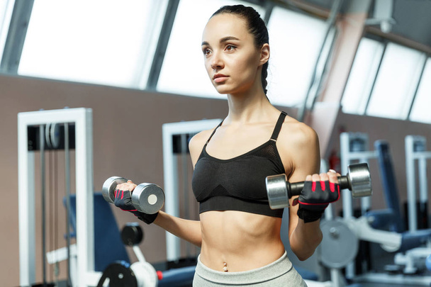 Young sporty woman exersises biceps with dumbells in a gym - Foto, Imagen