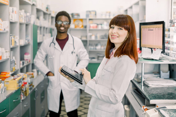 Portrait of a multiethnical male and female pharmacists smiling in front of medicines at drugstore - Photo, Image