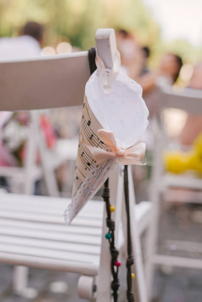 Бумажный пакет для лепестков роз для регистрации брака висит на спинке белого стула
 - Фото, изображение