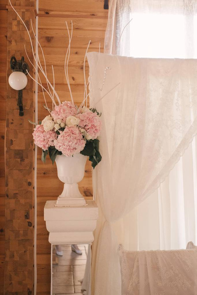 Цветочная композиция розовых гортензий стоит на декоративной колонне, украшающей свадебный банкет
 - Фото, изображение